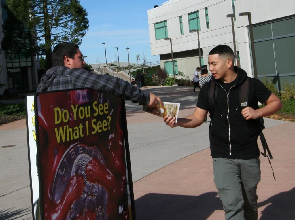 A staff member of the anti-abortion group, Survivors of the Abortion Holocaust, hands out literature to a passing Skyline student. (Denise Juarez)