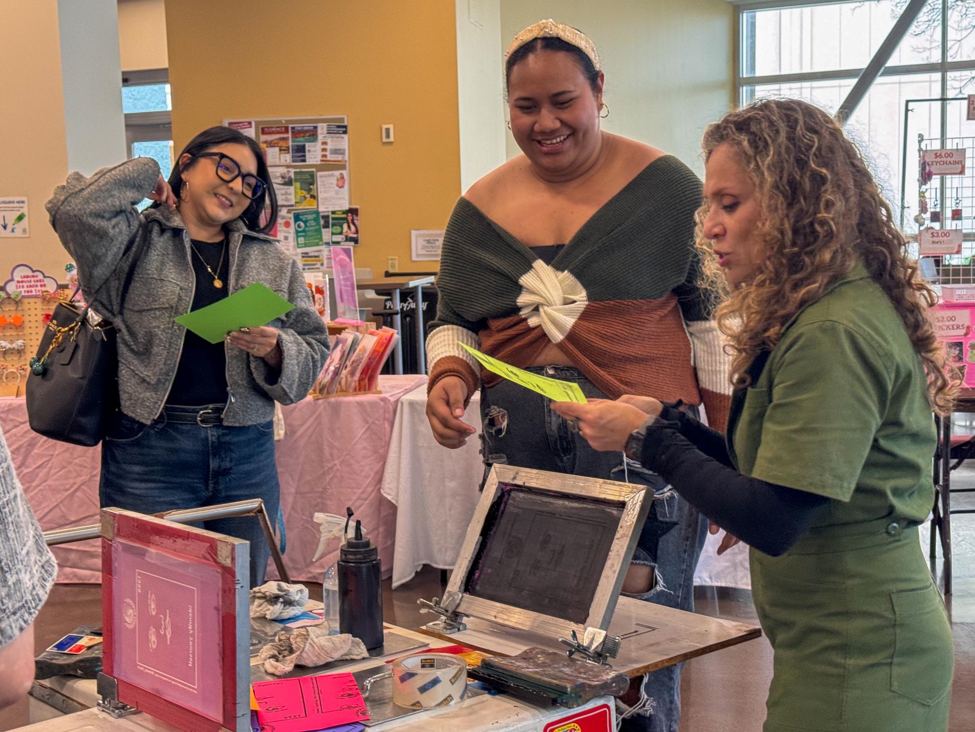 Angela Serrano and Toakase Toke listen to vendor Irene Caravajal as she explains screen printing.